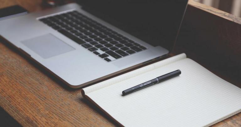 A laptop and notebook sitting on a wooden desk.