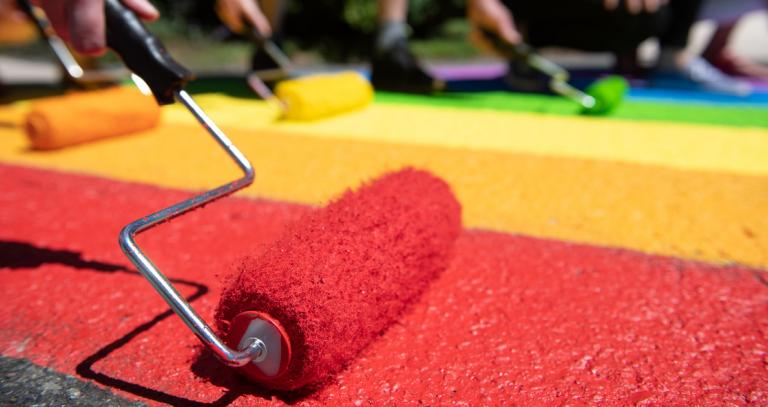 Paint rollers lined up in a row covering pavement in the Pride colours