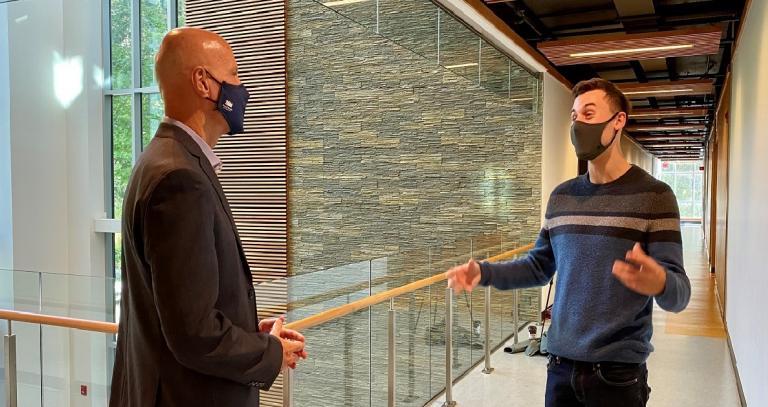 Student Riley Huntley speaks animatedly with President Philip Steenkamp in a bright glassy hallway, 