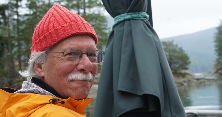 Richard Kool looking over his shoulder smiling next to a view of nature.