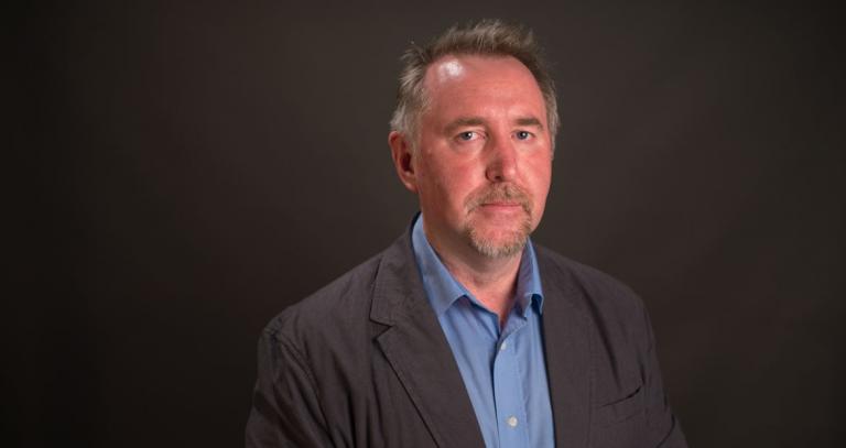 Prof. Ken Christie poses in a head-and-shoulders portriat against a black background.