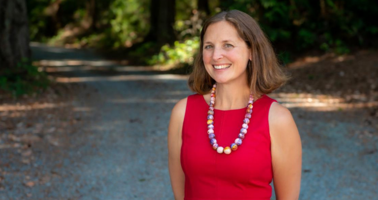 Cheryl Heykoop stands smiling at the camera on a forested path.