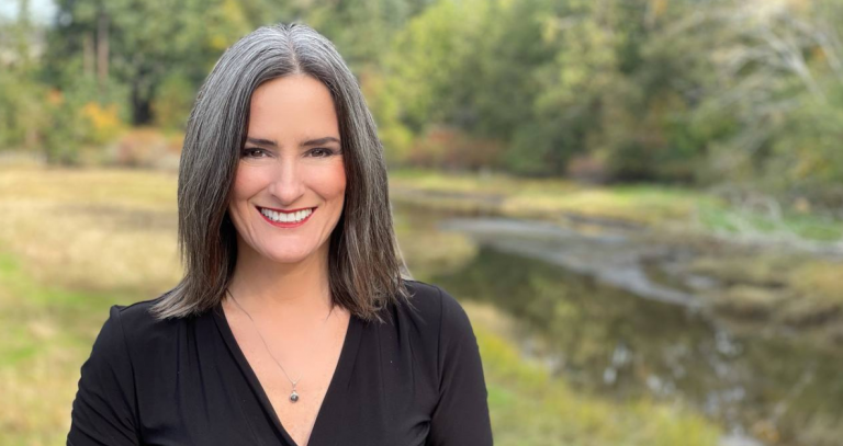 Head shot of Jill McAbe stanind in front of a grassy field surrounded by trees