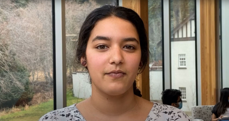 Cecilia, a Royal Roads student with brown hair and brown skin, shown in the Sherman Jen building on campus.