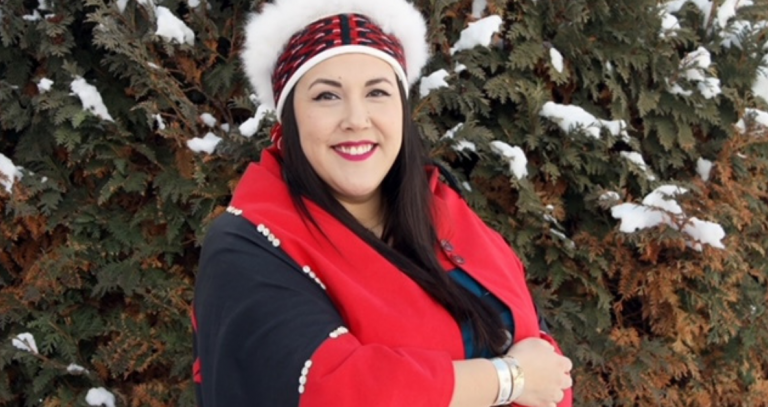 Juli Holloway is wrapped in a red and black blanket and wears a head piece. She looks happy.