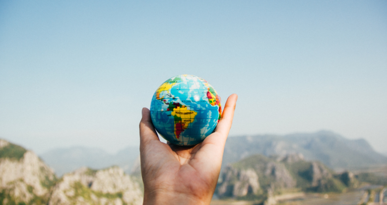 An outstretched hand holds a globe. Mountains can be seen in a distant background.