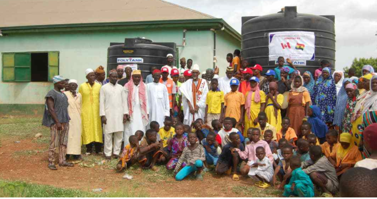 A large group of people pose in front of a water collection tank in Ghana.