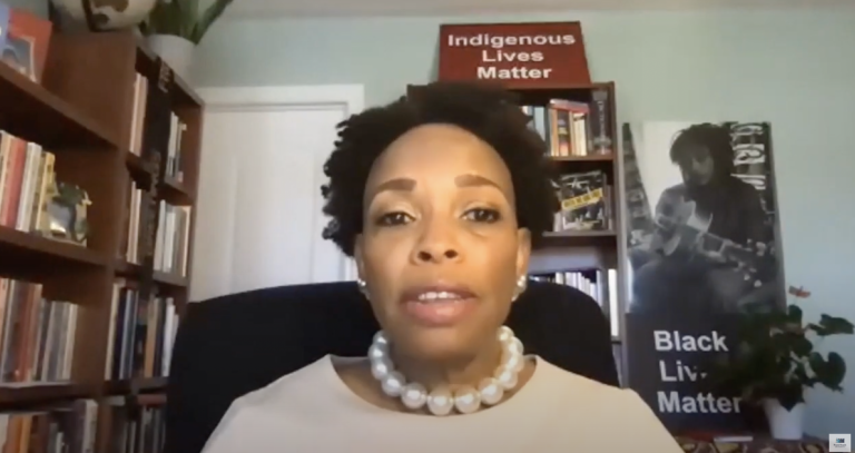 A screenshot of Prof. Andrea A. Davis delivering a talk from a room with many books and two signs that read "Black Lives Matter" and "Indigenous Lives Matter".