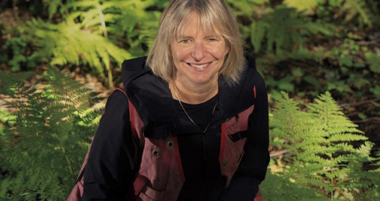 A woman smiles upwards towards a camera with a forested background.