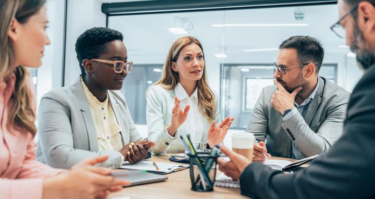 Five people in deep discussion around a conference table in an office setting.