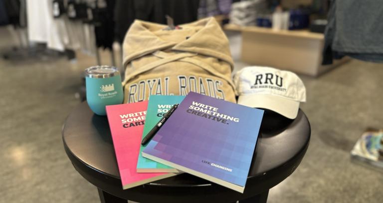 The poetry contest prize pack of a tan RRU hoody, white RRU ball cap, teal goblet style take-out mug, and an array of colourful notebooks.