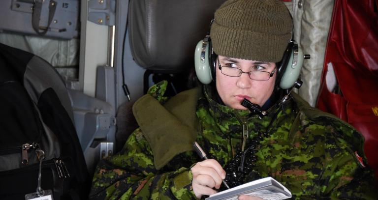Bettina McCulloch-Drake in Canadian Armed Forces uniform, wearing glasses and headphones and holding a notebook and pen. Photo credit: Mathieu Gaudreau.