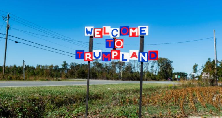 A sign that says "Welcome to Trump land" in front of a field