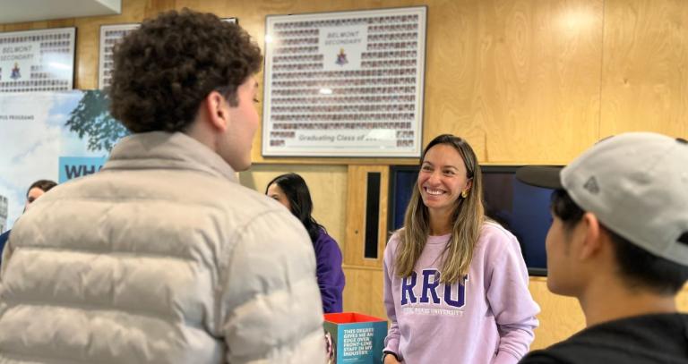 POV image over the shoulders of two high school students who are talking to a smiling RRU staffer wearing a lilac sweatshirt