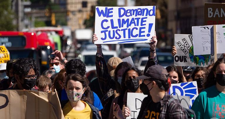 A group of protestors march, with a sign reading "We demand climate justice"