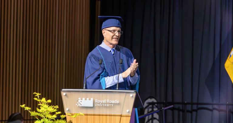 Philip Steenkamp standing on stage at Spring 2025 Convocation, wearing academic robe and clapping