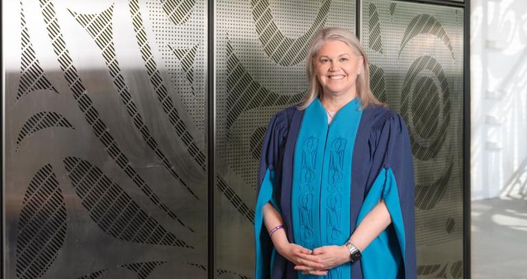 Jody Thomas stands outside of the Dogwood Auditorium wearing convocation robes.
