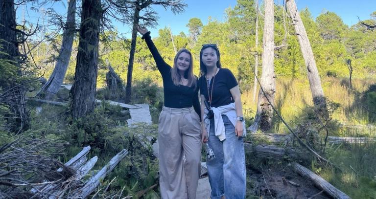 Two young students pose for a photo in a forested area.