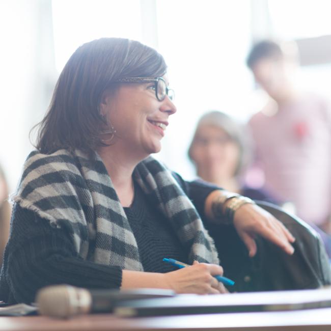 Student-with-scarf-and-glasses-smiling-with-pen-in-hand