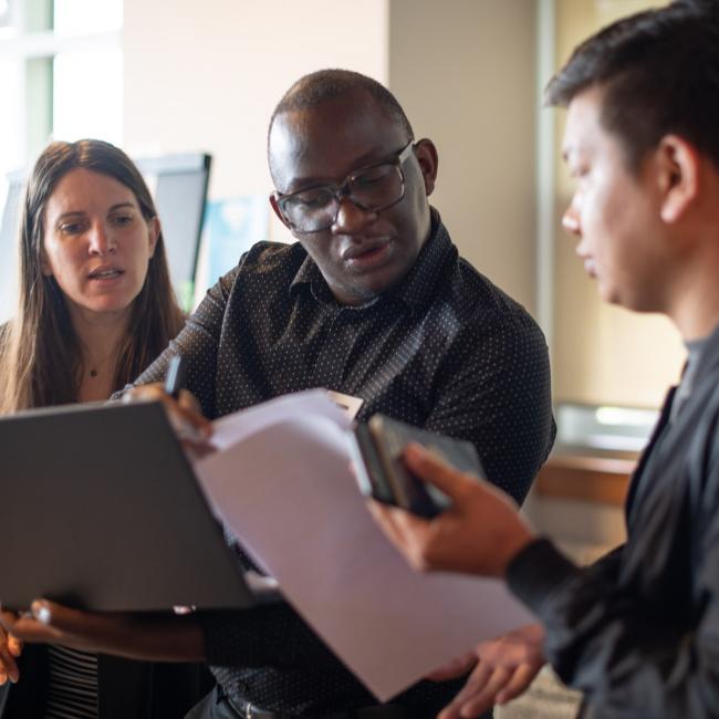 Three-students-looking-at-notes-and-laptop-together