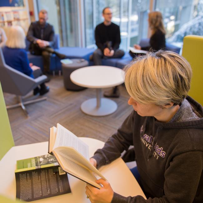 Student-reading-book-and-a-group-talking-in-the-background