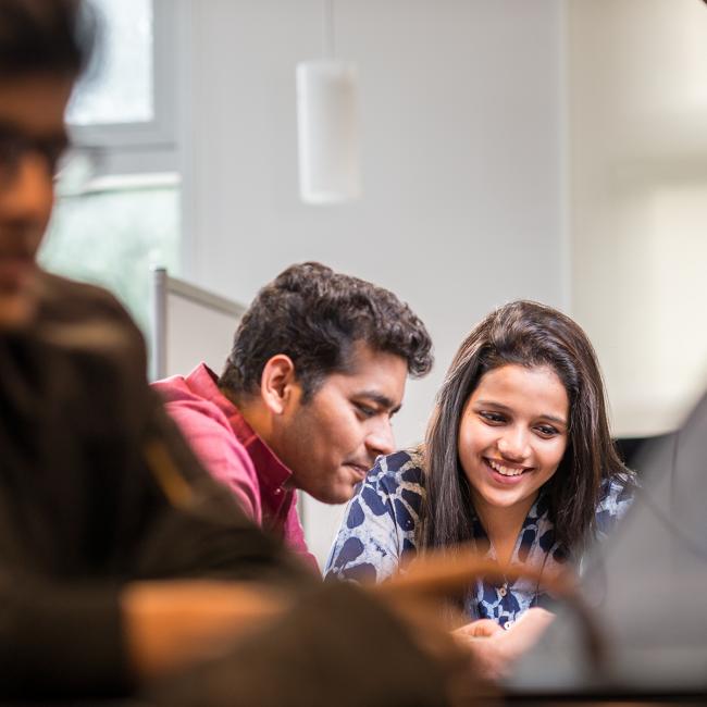 Two-students-leaning-over-a-table-smiling