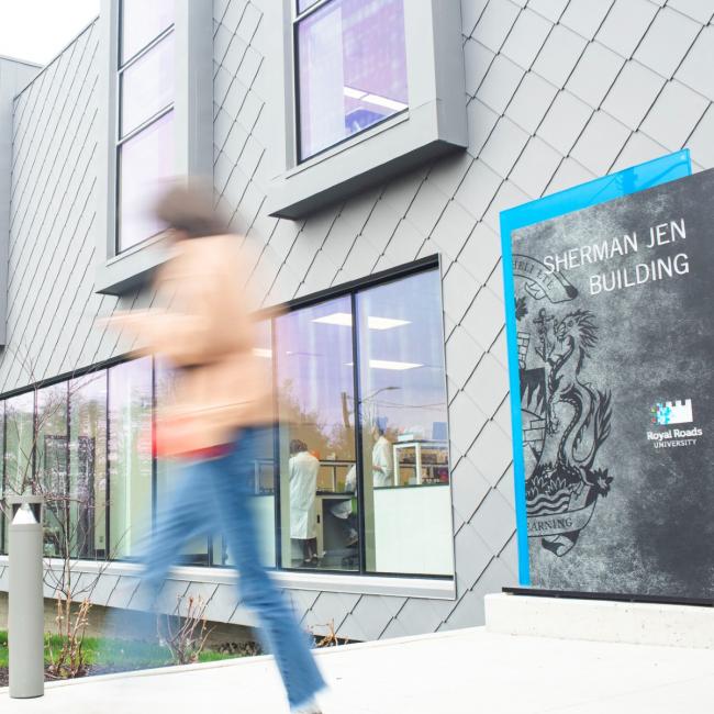 A blurred figure walks past the front of the Sherman Jen building