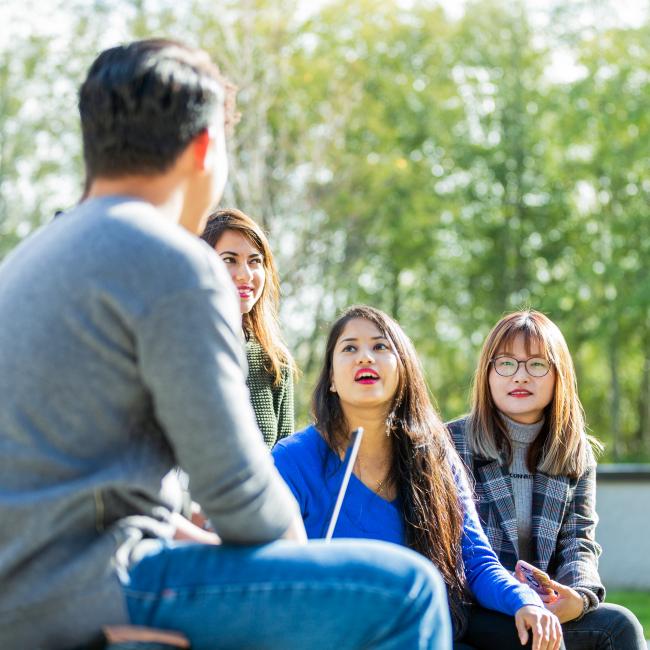 A group of students sits outside in the sun chatting.