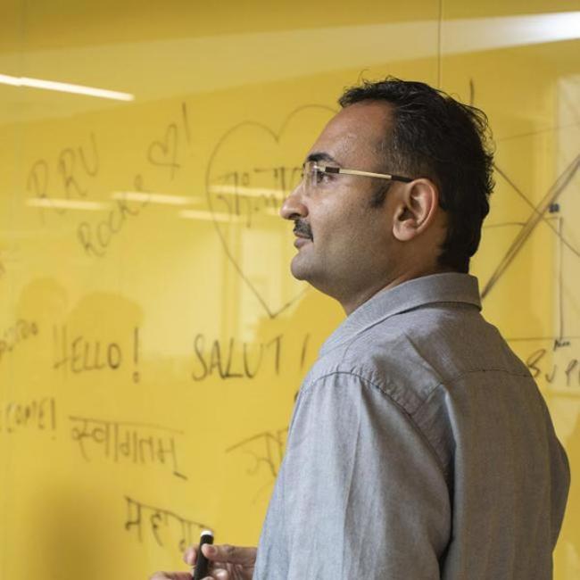 A student stands in front of their work on a white board while looking toward the class.