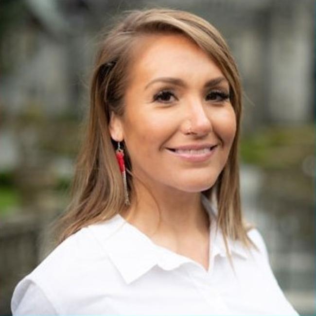 A woman in a white blouse looks directly at camera