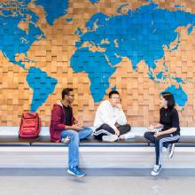 three-students-sitting-next-to-wood-panel-world-map